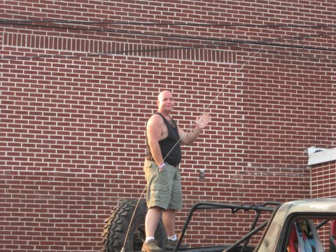 1984 Ford Bronco - A man stands atop an off-road vehicle, waving to the camera in front of a brick wall.