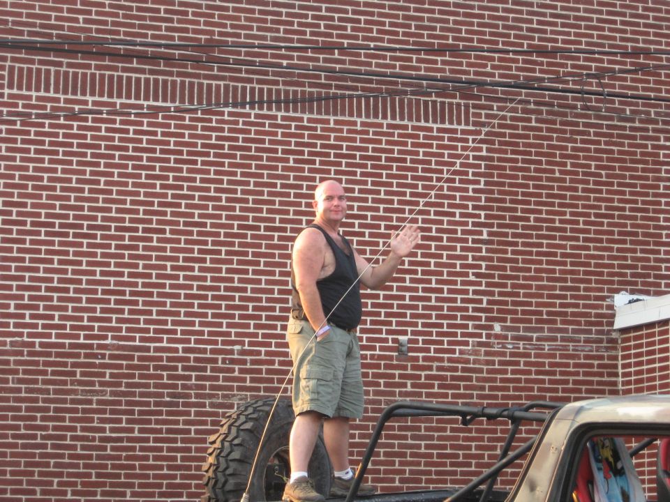 guy waving from top of off-road vehicle with spare tire
