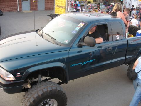 1984 Ford Bronco - A lifted dark teal pickup truck is parked outdoors, with a man visible in the driver's seat.