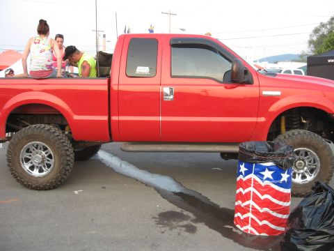 1984 Ford Bronco - A red pickup truck with a lifted suspension and chrome wheels is parked outdoors.