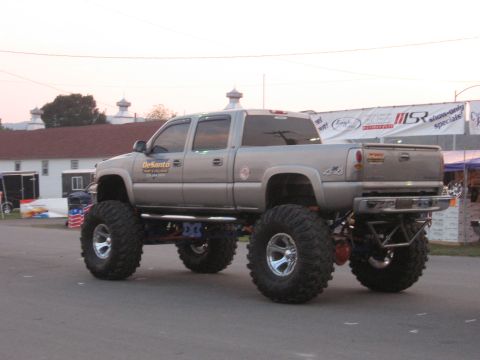 1984 Ford Bronco - A lifted pickup truck with oversized tires is parked outdoors, possibly at an event.