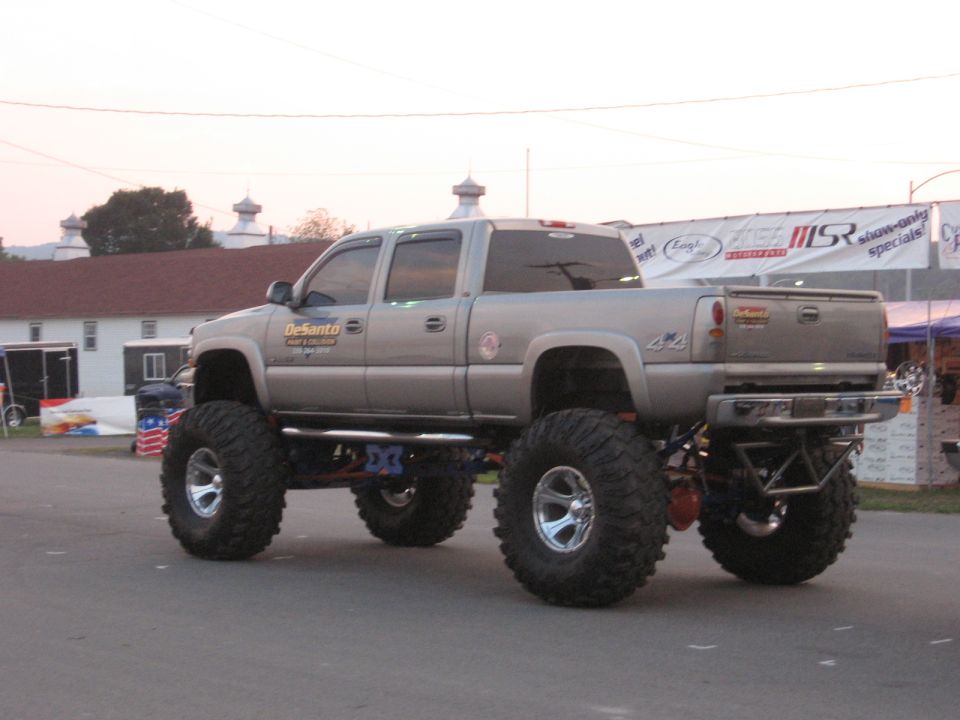 Silver lifted pickup truck with huge tires, 4x4 badge on the side
