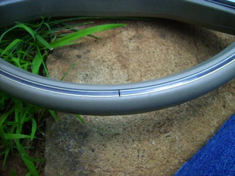 1982 Ford LTD Crown Victoria - Extreme close-up of a tan steering wheel rim resting on a concrete block beside grass, showing the thin chrome-look accent stripe and a hai…