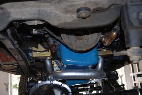 1975 Jeep CJ5 - The underside of a vehicle reveals its engine components, including the oil pan and exhaust system.