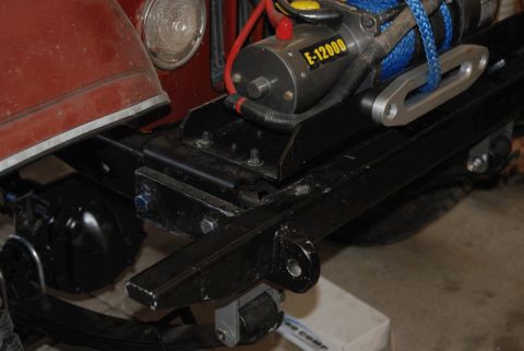 1975 Jeep CJ5 - A close-up view of an E-12000 winch mounted on a vehicle's black frame.