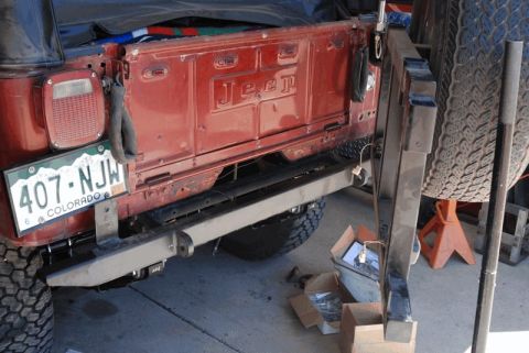 1975 Jeep CJ5 - The rear of a red Jeep is shown, with a spare tire and license plate visible. Parts are in boxes nearby.