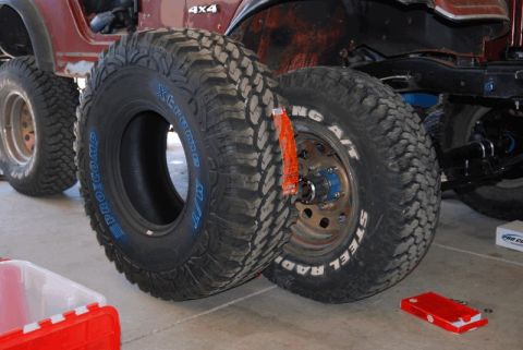 1975 Jeep CJ5 - Two large off-road tires are shown in front of a red Jeep CJ, with one tire mounted on a wheel.