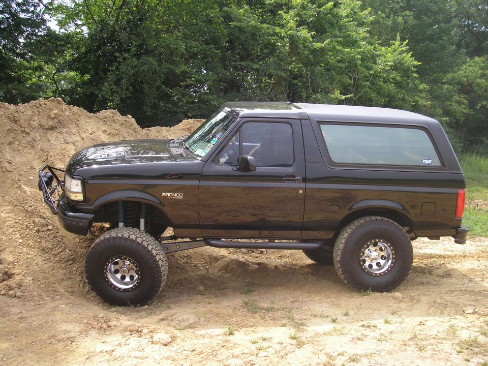 Black lifted two-door Ford Bronco SUV in side view on dirt with off-road tires