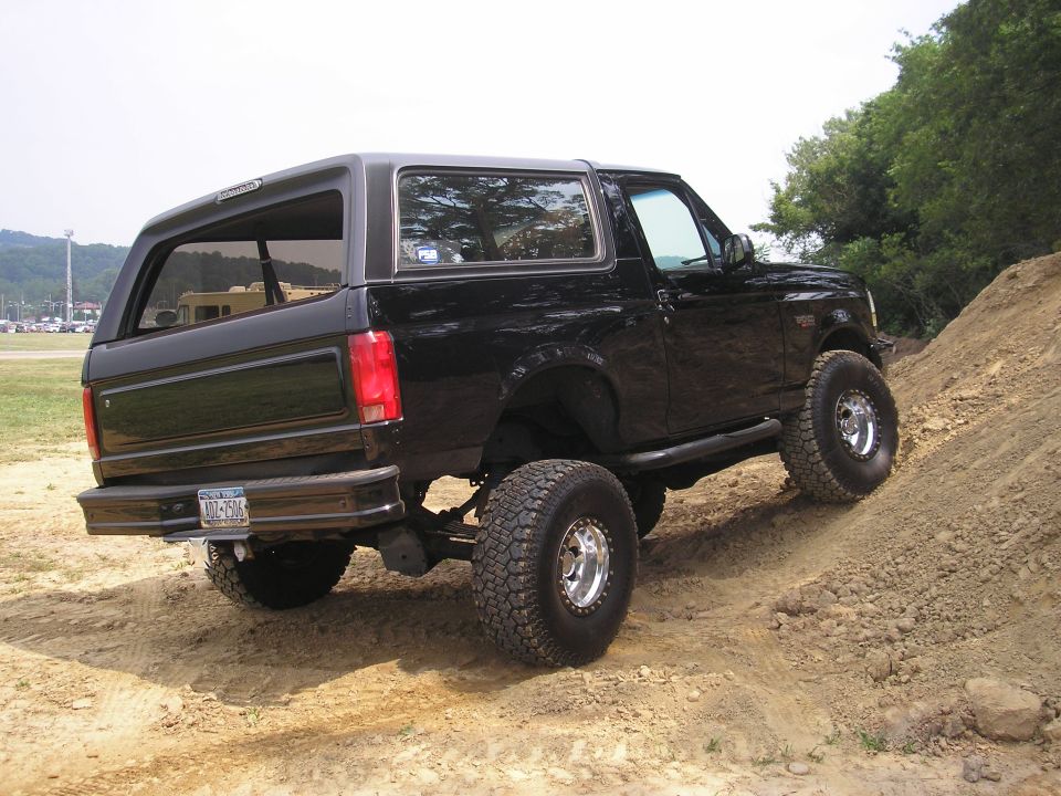 Black lifted Ford Bronco SUV climbing dirt hill, rear 3/4 view with off-road tires