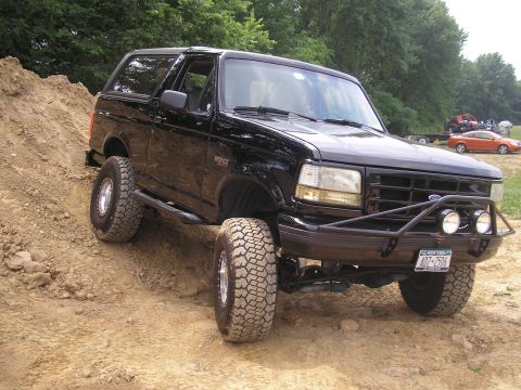 1995 Ford Bronco - Black 1995 Ford Bronco navigating an off-road course with large tires.