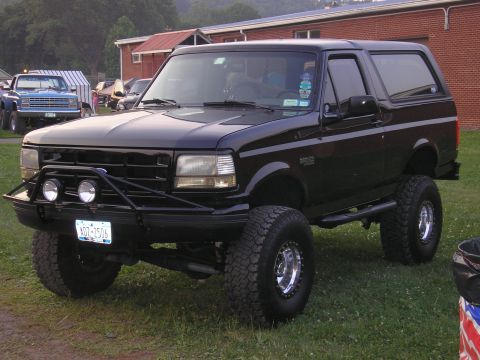 1995 Ford Bronco - A lifted black Ford Bronco sits on a grassy field with other vehicles in the background.