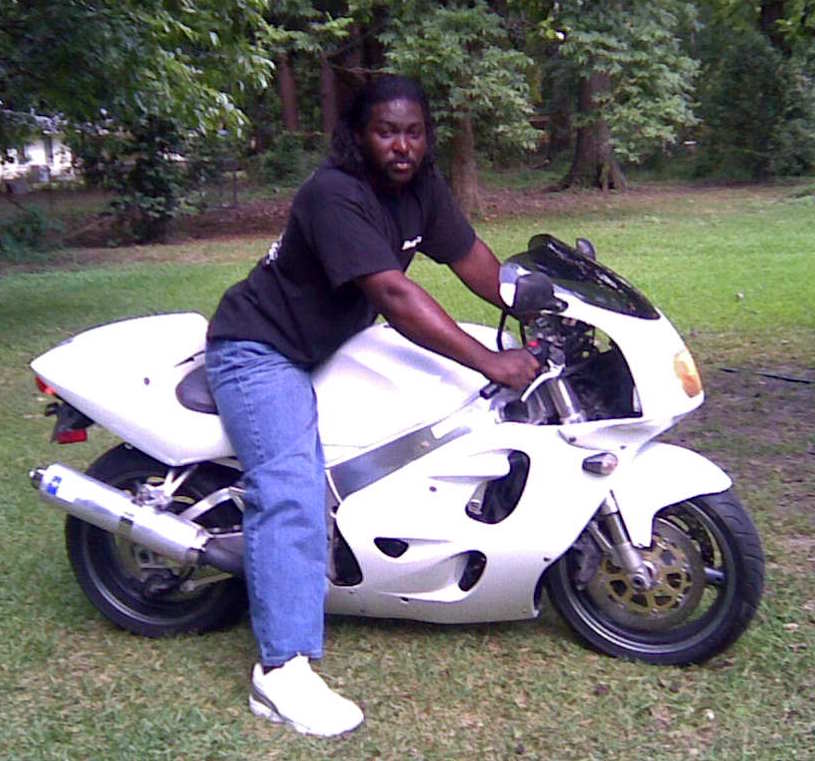 Man straddling a white sportbike motorcycle on a lawn