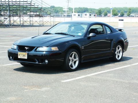 2001 Mercury Grand Marquis - A black Ford Mustang is parked in an asphalt lot with bleachers in the background.
