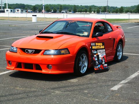 2001 Mercury Grand Marquis - A bright orange 2004 Ford Mustang is parked at an outdoor car show.