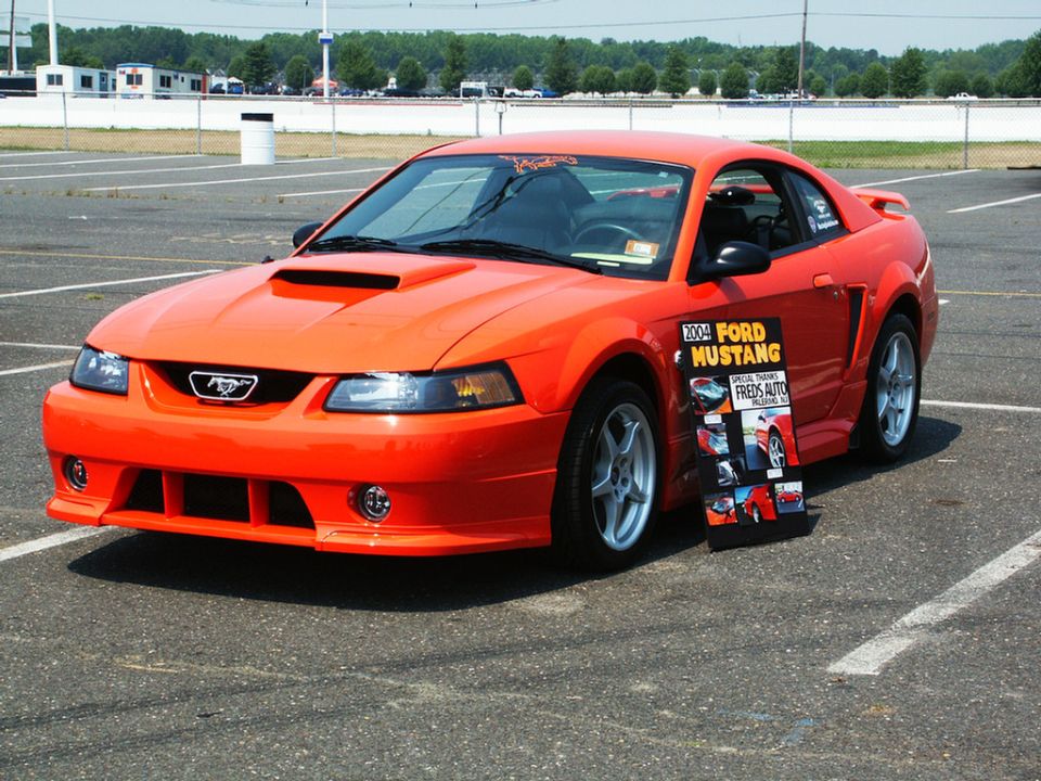 Orange 2004 Ford Mustang coupe with a hood scoop and a display board on its side