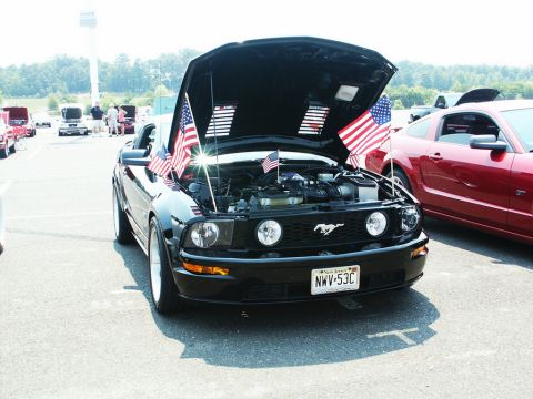 2001 Mercury Grand Marquis - Black Ford Mustang on display with hood open, American flags and parked next to a red Mustang.