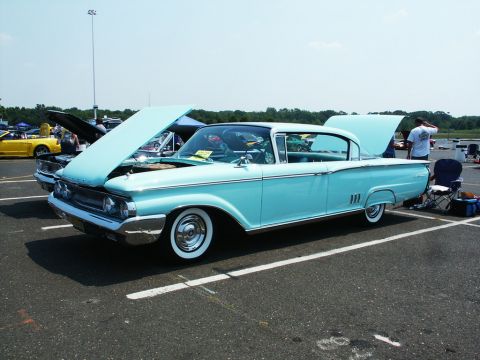 2001 Mercury Grand Marquis - Light-blue 1960 Mercury two-door hardtop with whitewall tires and hood raised at an outdoor car-show lot.