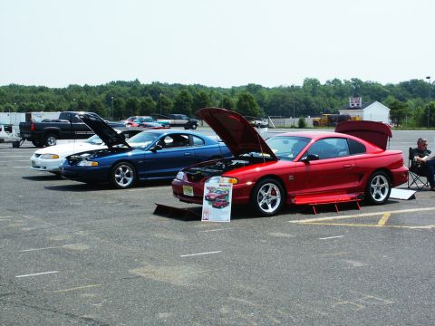 2001 Mercury Grand Marquis - A red coupe, likely a Ford Mustang from the mid-1990s, is displayed with its hood open at a car show.