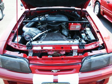 2001 Mercury Grand Marquis - The engine bay of a red car is open, revealing a supercharger and other engine components. Another red car is visible in the background.