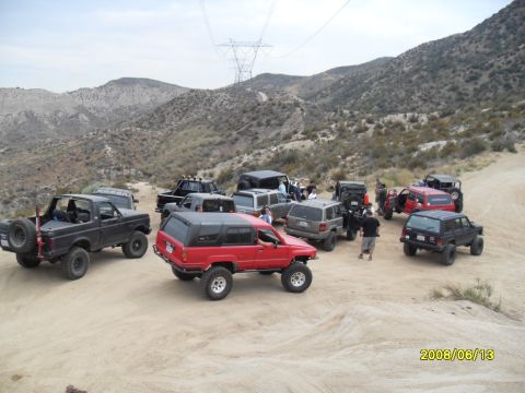 1990 Ford Bronco - Multiple off-road vehicles parked on a dirt path in a mountainous, arid landscape.