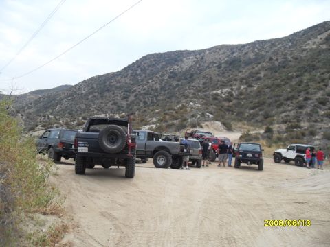1990 Ford Bronco - A group of vehicles gathered on a dusty trail, with people milling around.