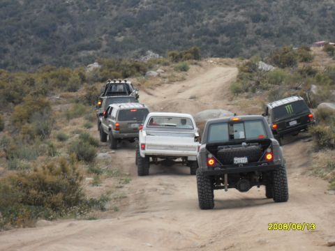 1990 Ford Bronco - A convoy of off-road vehicles navigates a dusty trail through a dry, hilly landscape.