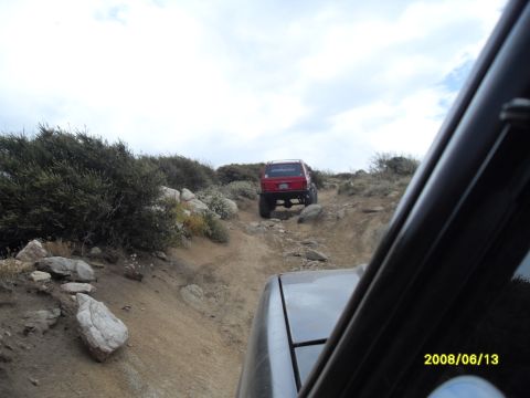 1990 Ford Bronco - Two vehicles navigate a challenging off-road trail under a cloudy sky.