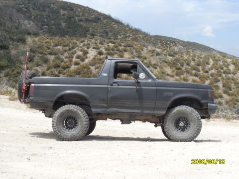 1990 Ford Bronco - A dark gray Ford Bronco is parked on a dirt road with a hilly, brush-covered landscape in the background.