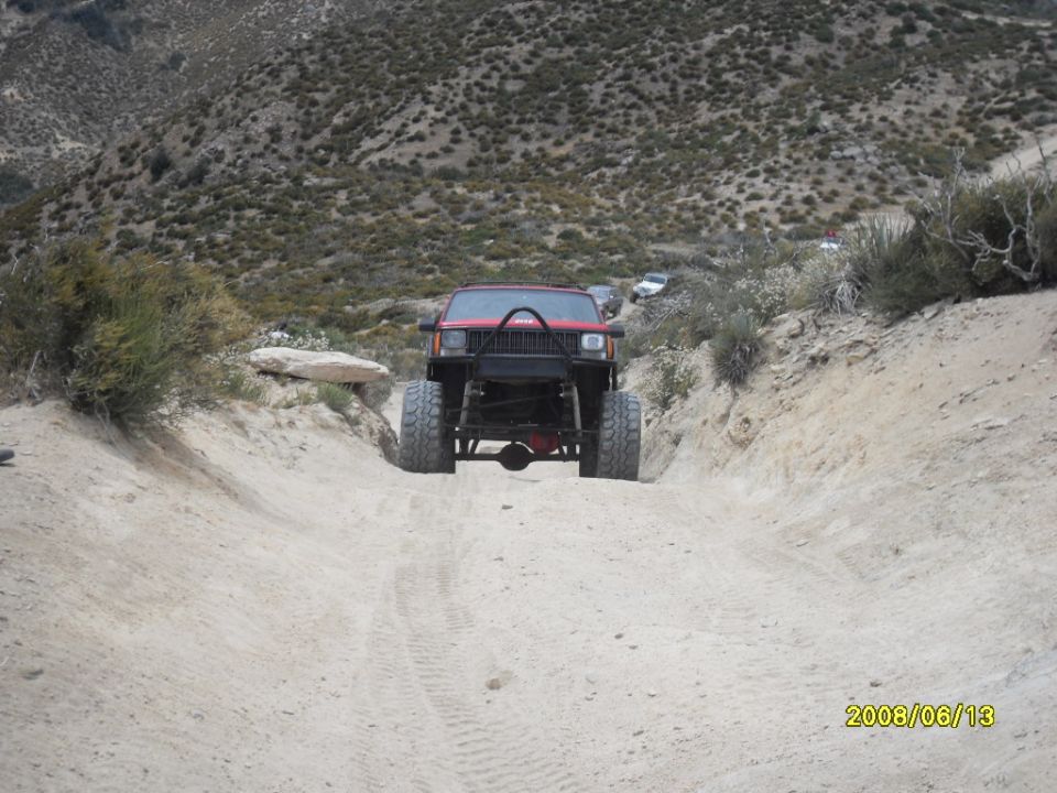 Red off-road SUV with large tires and a roll cage driving on a dirt road