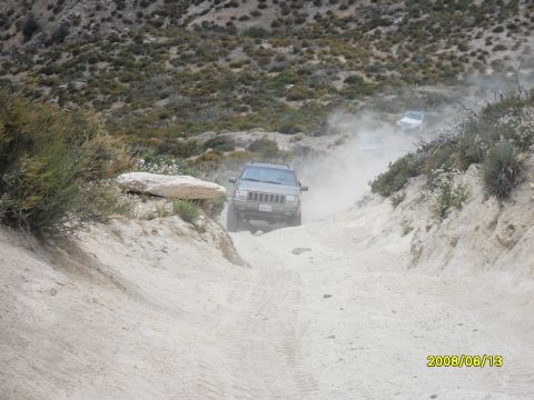 1990 Ford Bronco - Multiple SUVs navigate a dusty off-road trail on a sunny day.