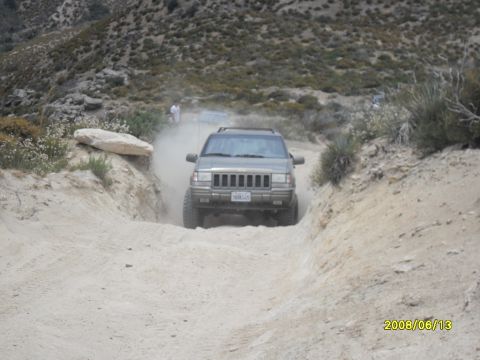 1990 Ford Bronco - A gray Jeep Grand Cherokee navigates a dusty off-road trail, with another vehicle visible in the background.