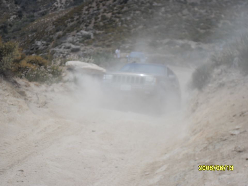 Jeep Grand Cherokee driving on a dusty dirt road, another vehicle visible in background