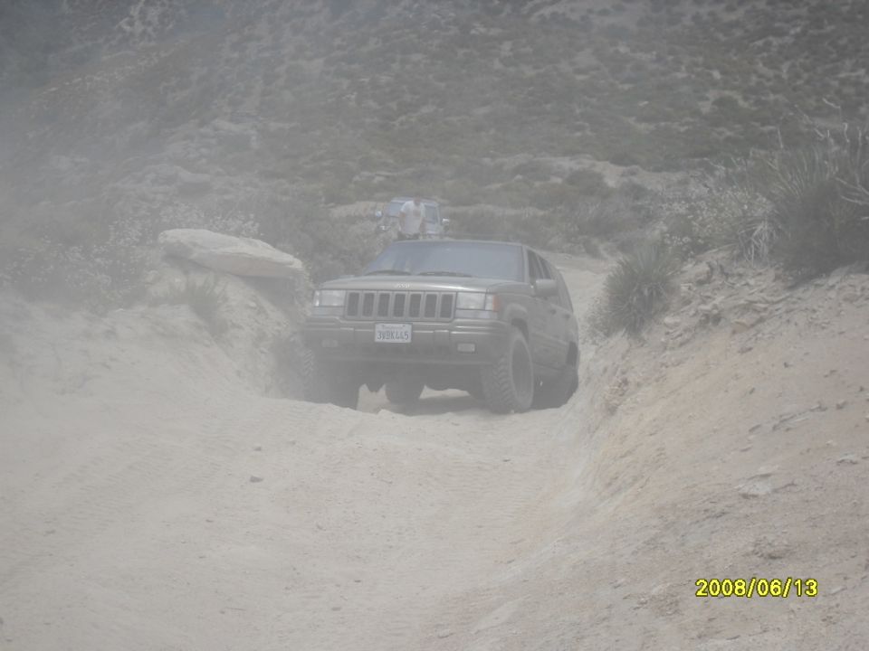 Jeep Grand Cherokee driving on a dusty dirt road, another vehicle is visible behind it