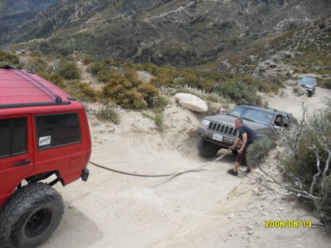 1990 Ford Bronco - Two SUVs are on a dirt road, one being towed by a man.