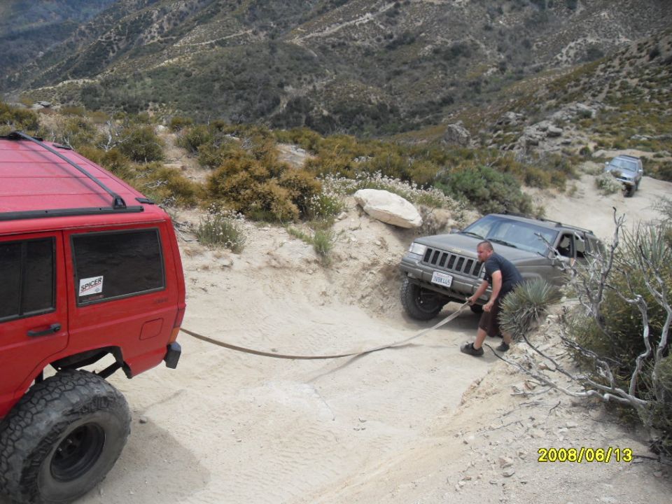 Red SUV rear, green Jeep Grand Cherokee being towed by a man on a dirt road