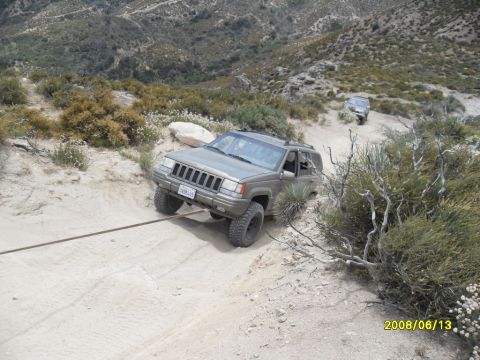 1990 Ford Bronco - Two Jeep Grand Cherokees navigate a challenging off-road trail with one vehicle being towed.