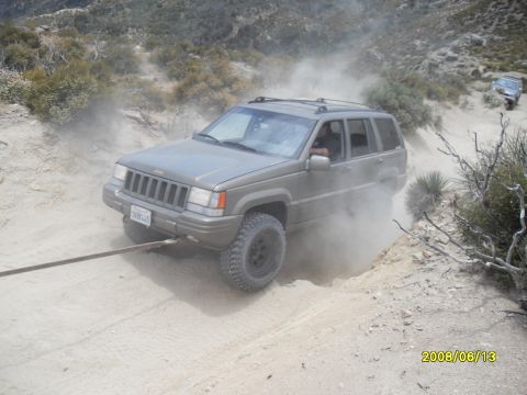 1990 Ford Bronco - A Jeep Grand Cherokee navigates a dusty off-road trail, with another vehicle in the distance.