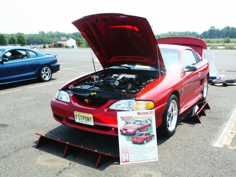 2001 Mercury Grand Marquis - A red 1994 Mustang GT is displayed with its hood open, alongside a blue Mustang at an outdoor car show.