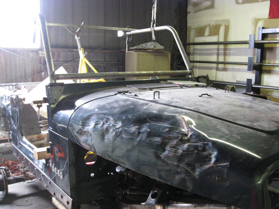 Jeep body with significant damage to the hood and fender, undergoing repairs in a workshop