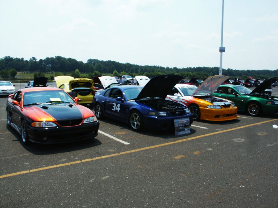 Orange and black Ford Mustang with hood open, parked at a car show