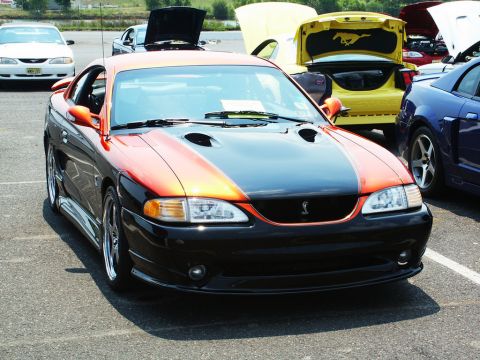 2001 Mercury Grand Marquis - A two-tone orange and black 1996 Ford Mustang Cobra is displayed at a car show, with other vehicles visible in the background.