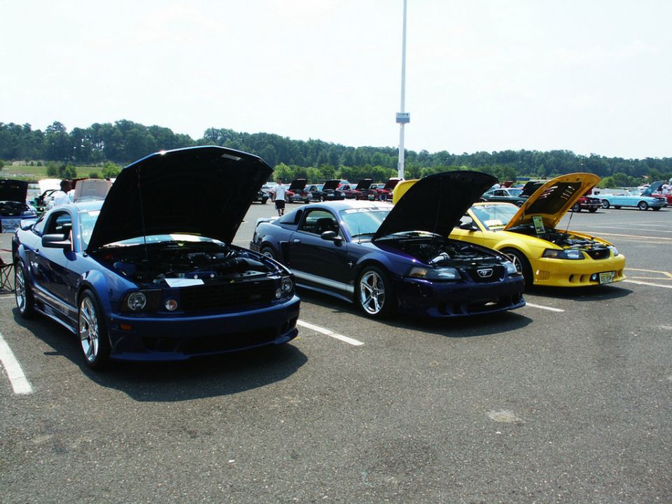 Three Ford Mustangs parked in a lot, hoods up. Blue, dark blue, and yellow