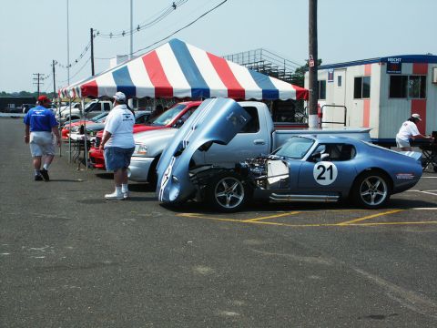2001 Mercury Grand Marquis - A blue race car with its hood open is displayed at a car show, alongside other vehicles and a tent.