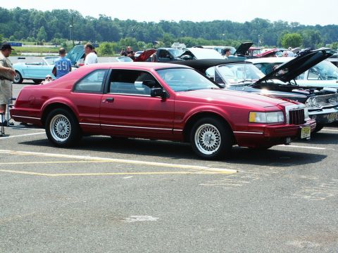 2001 Mercury Grand Marquis - Red coupe with wire wheels at a car show, other cars in background.