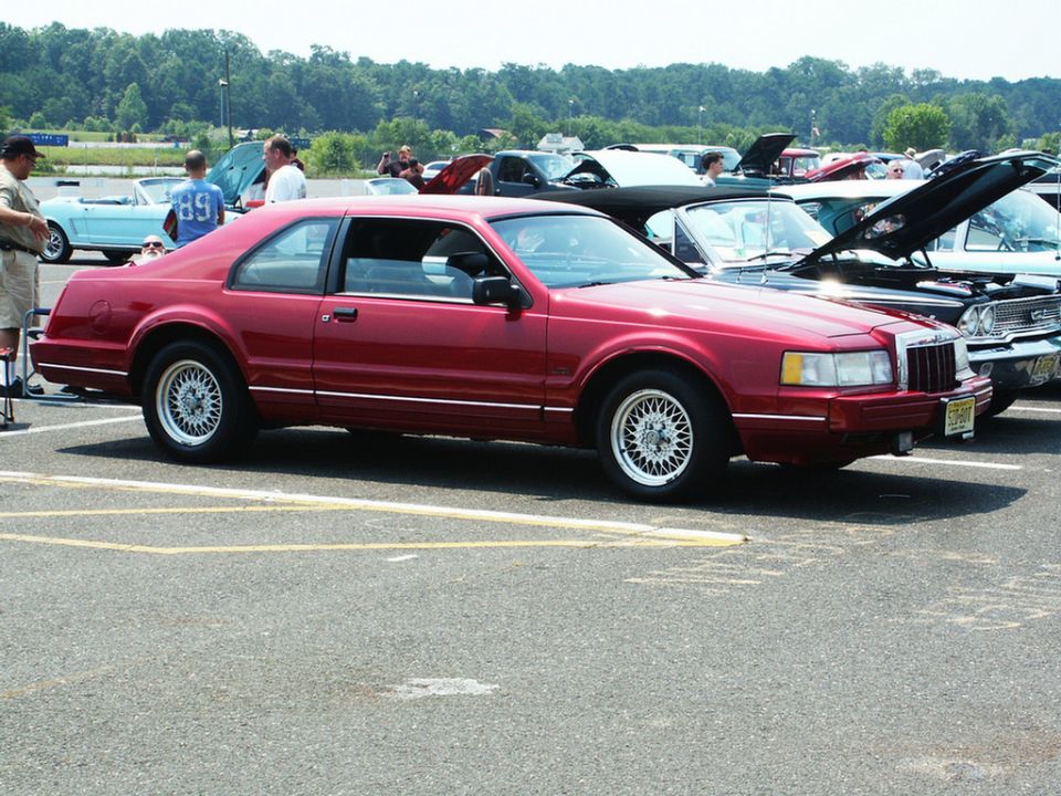 Red coupe with wire wheels parked at a car show, other vehicles visible