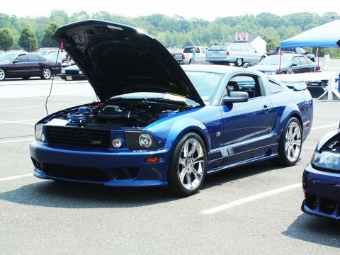 2001 Mercury Grand Marquis - A blue Ford Mustang is displayed with its hood open at an outdoor car show, with other vehicles in the background.