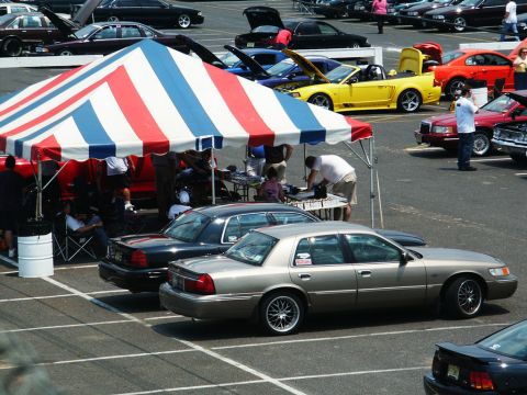 2001 Mercury Grand Marquis - Elevated view of a gold Mercury Grand Marquis sedan on chrome multi-spoke wheels parked beside a black Crown Victoria at an outdoor car sho…
