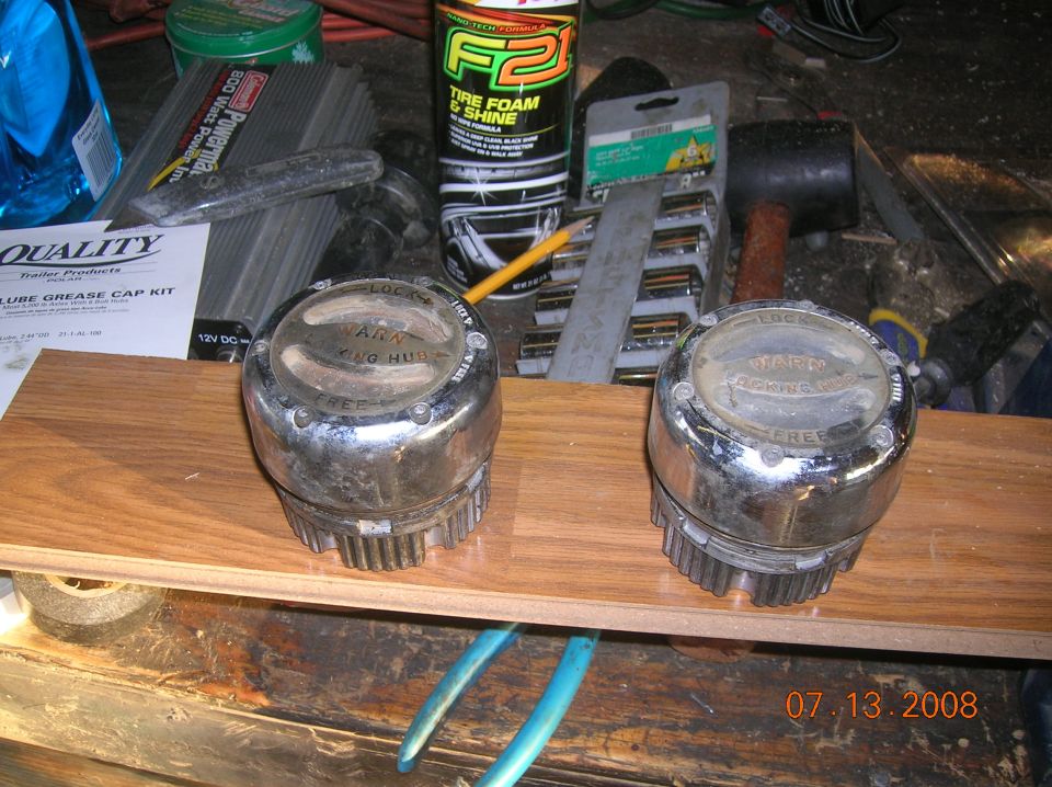 Two chrome manual locking hubs with 'WARN' and 'KING HUB' text, resting on a wooden plank