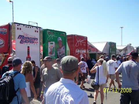 1972 Ford Ranchero - People mill about in a pit area, passing large trailers displaying various racing sponsors and drivers.