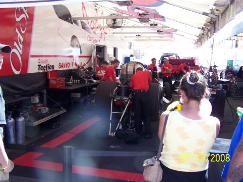1972 Ford Ranchero - A drag racing pit crew is seen working on a vehicle in a garage bay. A trailer with branding is in the background.